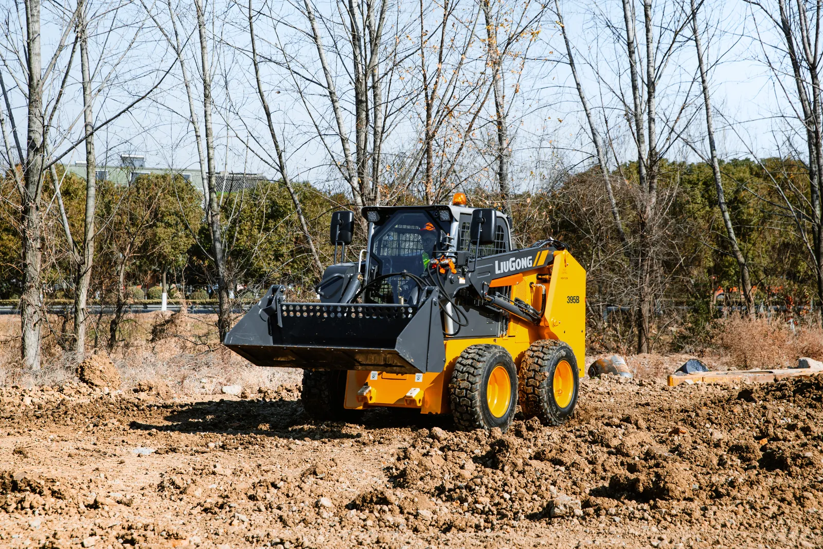 Mini carregadeira LiuGong nivelando terreno com a caçamba rente ao solo.